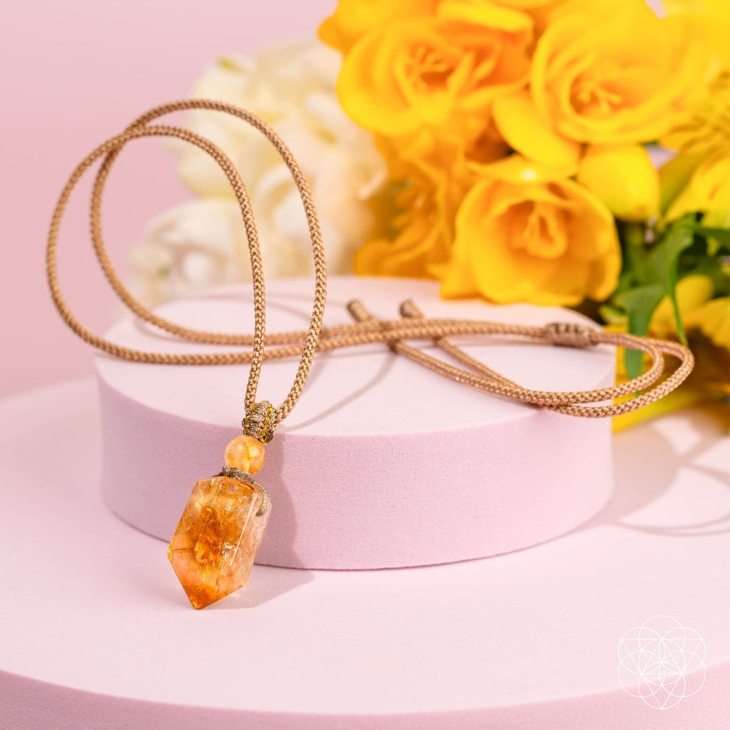 Necklace with a yellow crystal pendant on a pink stand with yellow flowers in the background